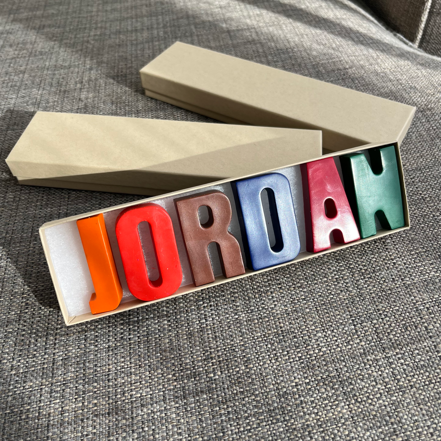 name JORDAN in crayons presented in a craft box. J is orange, O is red, R is brown, D is blue, A is burgundy, N is green 